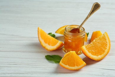 Jar of sweet orange jam and mint on white wooden table, space for text