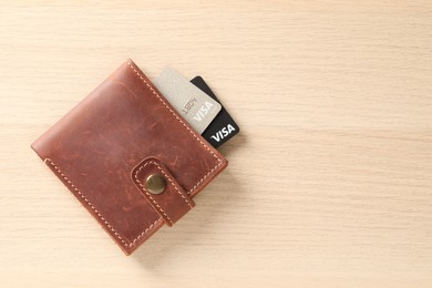 MYKOLAIV, UKRAINE - FEBRUARY 23, 2022: Bank cards of Visa payment system in leather wallet on wooden table, top view. Space for text