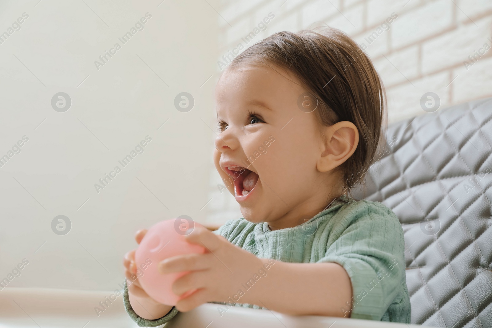 Photo of Cute little baby nibbling toy in high chair indoors. Space for text