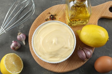 Photo of Fresh mayonnaise sauce in bowl and ingredients on grey table, flat lay