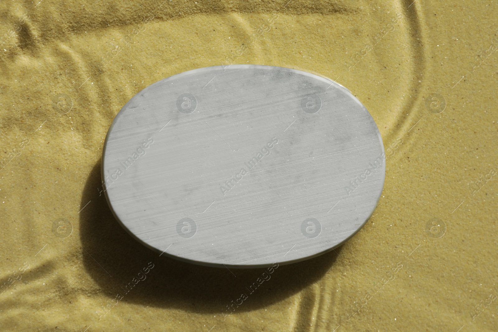 Photo of Stylish presentation for product. Stone podium in water on sand, top view