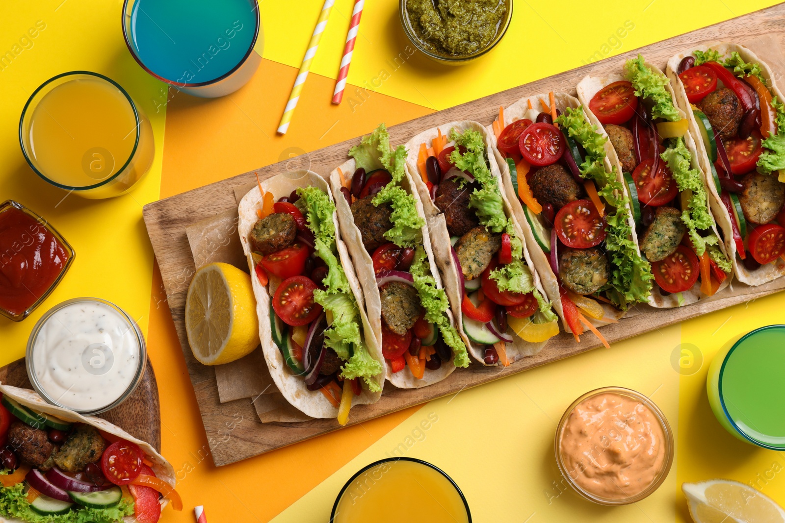 Photo of Many delicious vegetarian tacos served on yellow table , flat lay