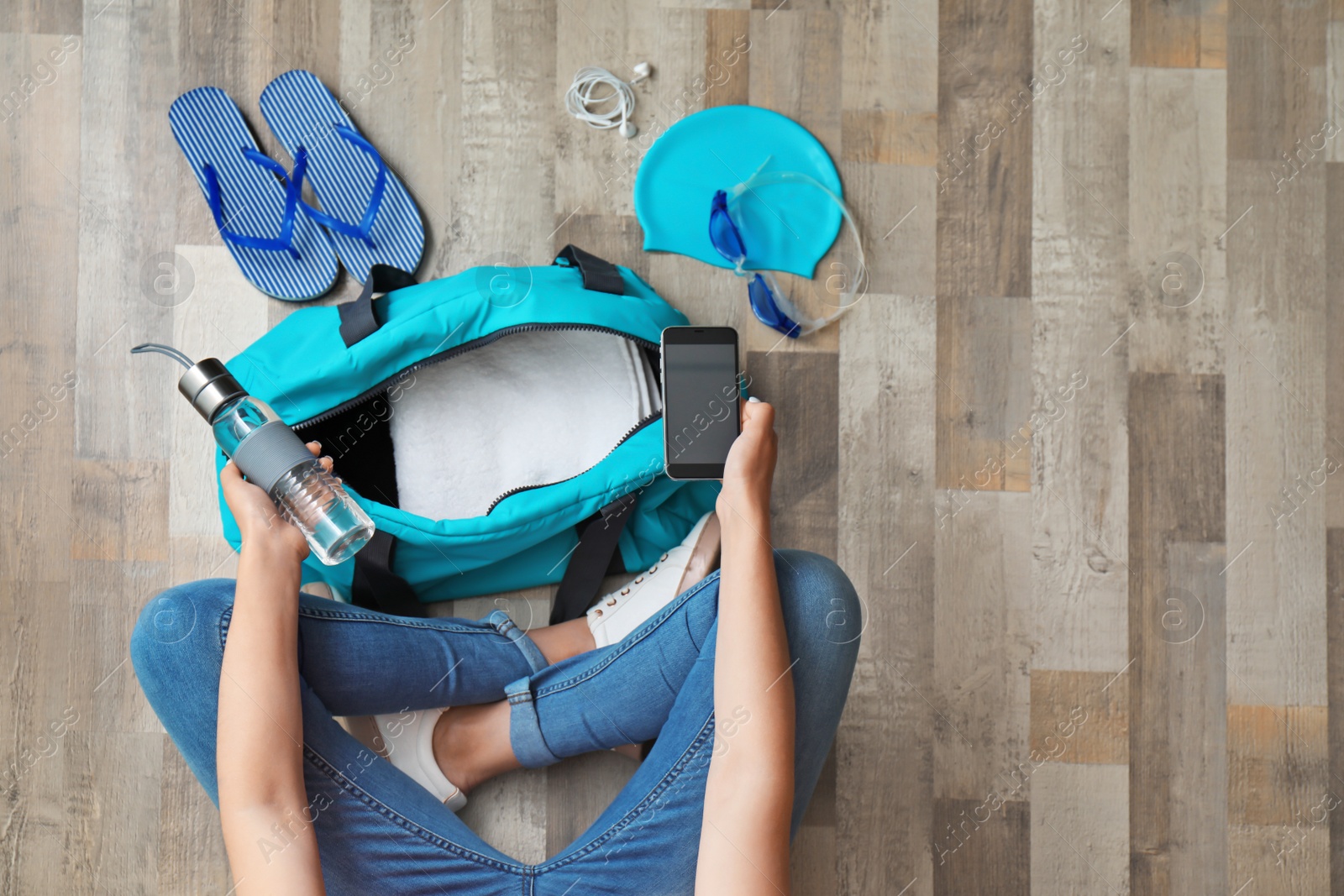 Photo of Young woman packing sports bag on floor, top view