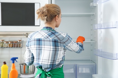 Woman in rubber gloves cleaning empty refrigerator at home