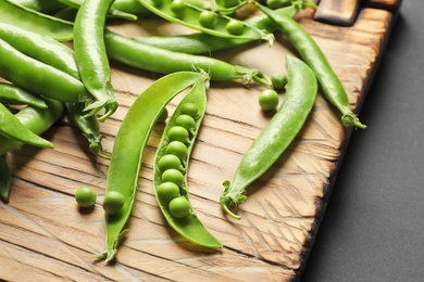 Photo of Wooden board with green peas on black background, closeup