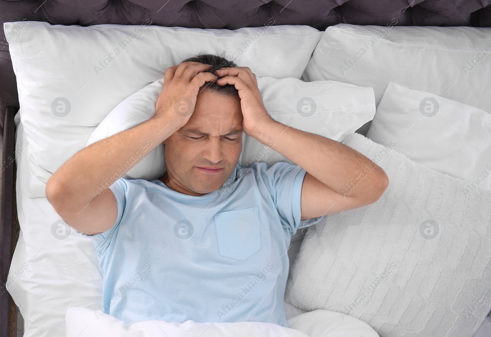 Photo of Man suffering from headache after sleep in bed. Uncomfortable pillow