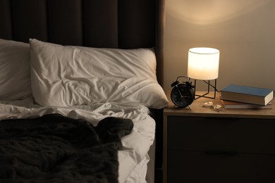 Nightlight, alarm clock, glasses and books on bedside table near bed indoors