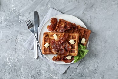 Photo of Delicious Belgium waffles served with fried bacon and butter on grey table, flat lay