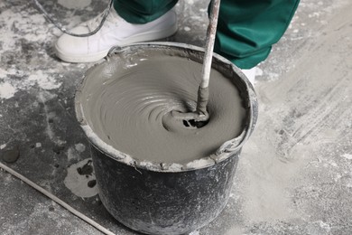 Photo of Worker mixing concrete in bucket indoors, closeup