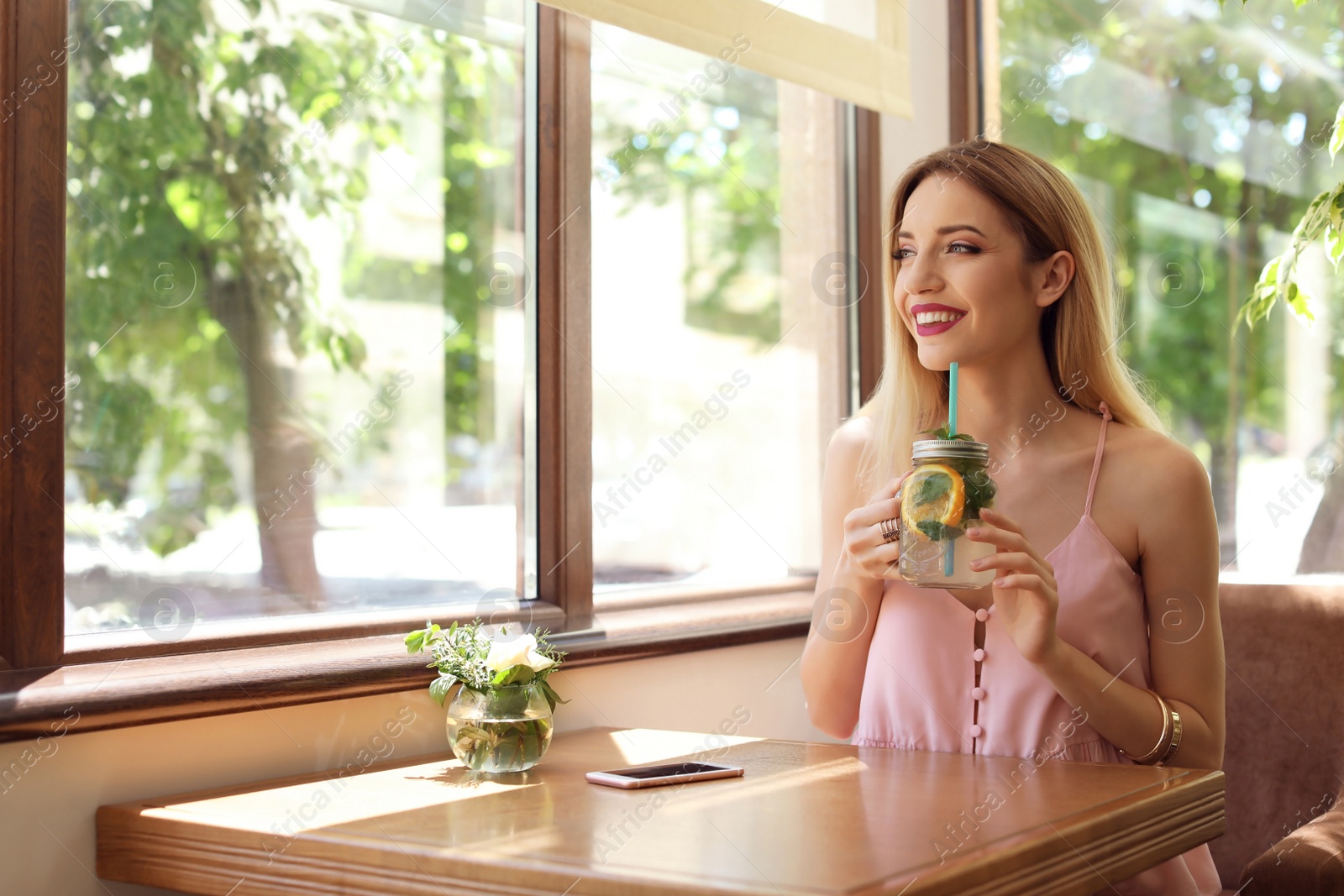Photo of Young woman with mason jar of tasty natural lemonade at table in cafe. Detox drink