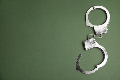 Photo of Classic chain handcuffs on dark green background, top view. Space for text