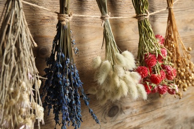 Photo of Bunches of beautiful dried flowers hanging on rope near wooden wall, closeup