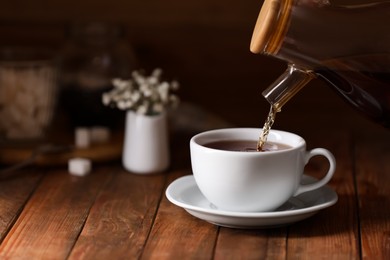 Photo of Pouring delicious tea into cup on wooden table, closeup. Space for text