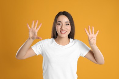 Photo of Woman in white t-shirt showing number nine with her hands on yellow background