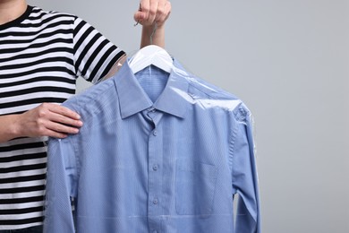 Dry-cleaning service. Woman holding shirt in plastic bag on gray background, closeup. Space for text