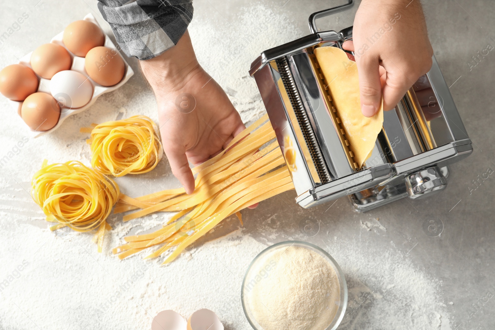 Photo of Young man preparing noodles with pasta maker at table, top view