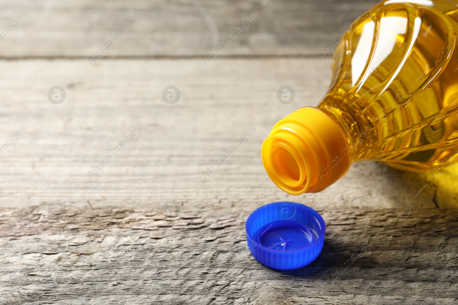 Photo of Plastic bottle of cooking oil on wooden table. Space for text