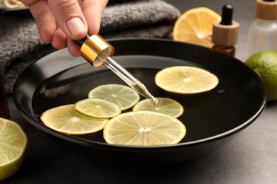Photo of Woman dripping essential oil into bowl with lemons at grey table, closeup. Aromatherapy treatment