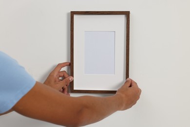 Young man hanging picture frame on white wall indoors, closeup