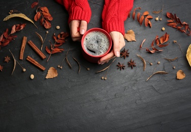 Photo of Woman with cup of hot drink at black table, top view with space for text. Cozy autumn atmosphere