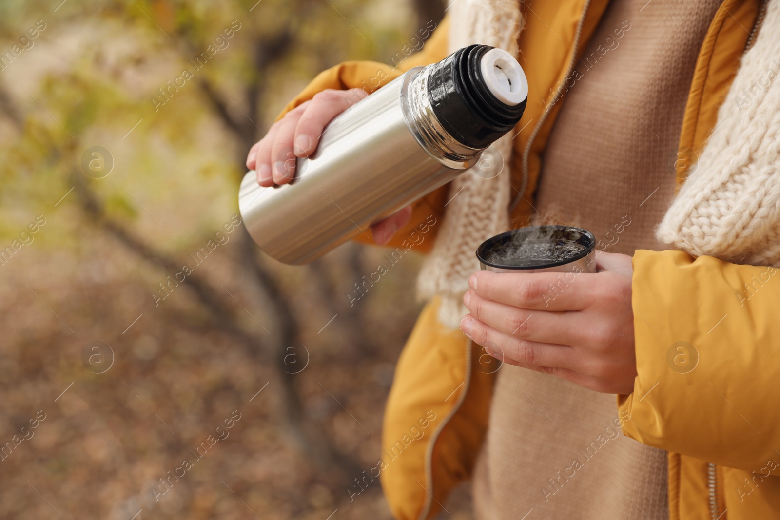 Photo of Woman pouring drink from thermos into cap outdoors, closeup