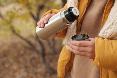 Photo of Woman pouring drink from thermos into cap outdoors, closeup