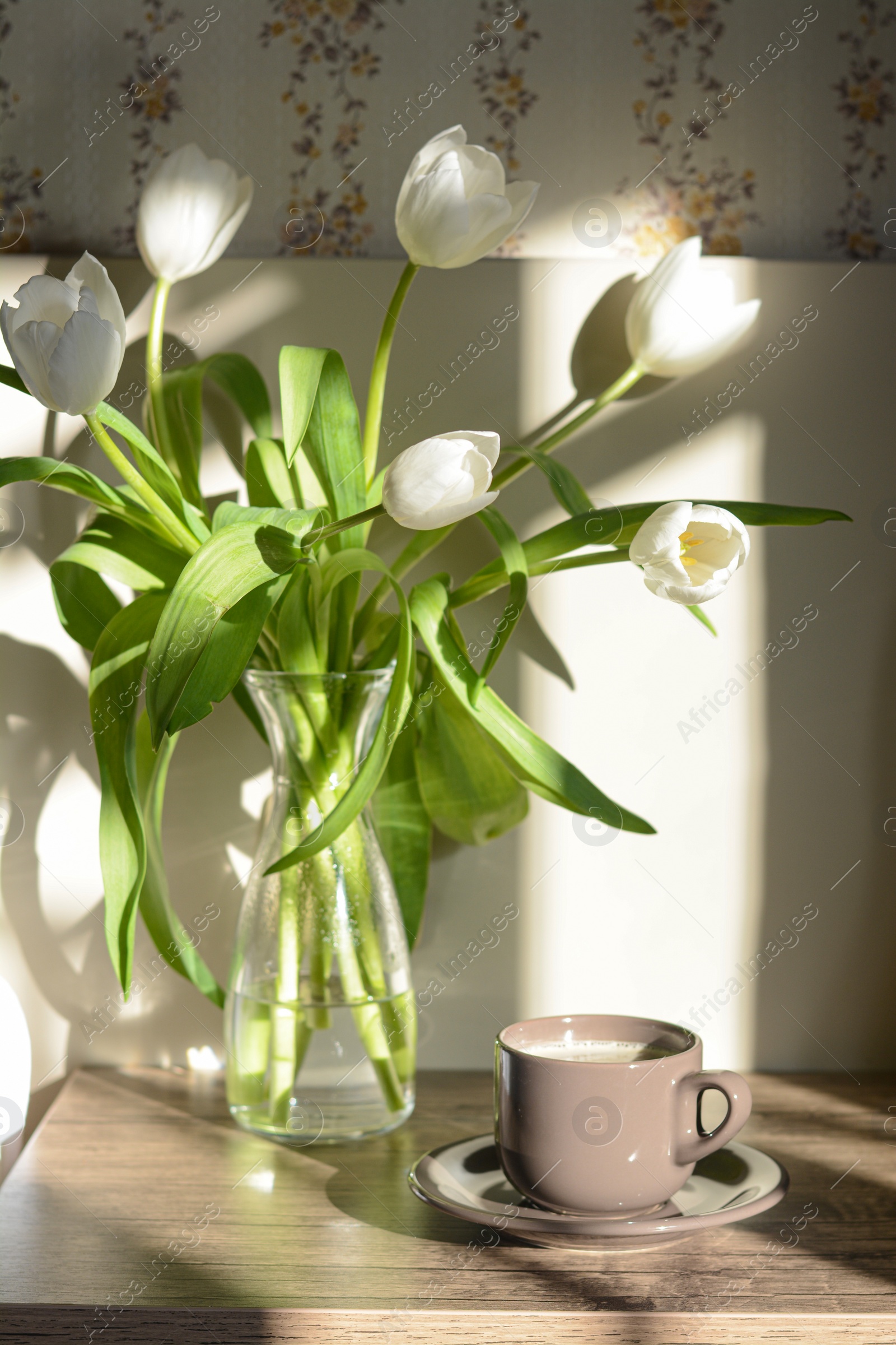 Photo of Beautiful white tulip bouquet and cup of coffee on wooden table indoors