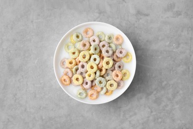 Photo of Tasty colorful cereal rings and milk in bowl on grey table, top view