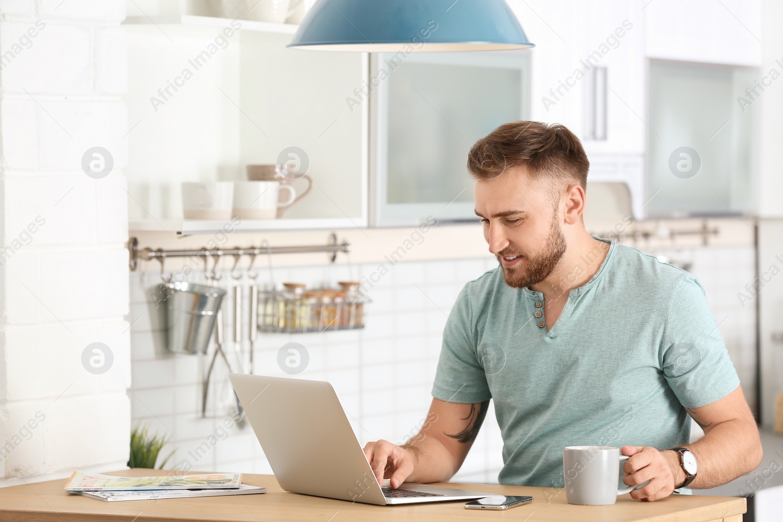 Photo of Young man using laptop at table in kitchen