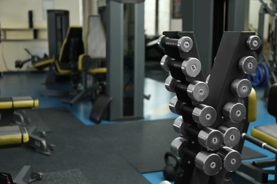 Photo of Dumbbells on rack in gym, space for text. Modern sport equipment