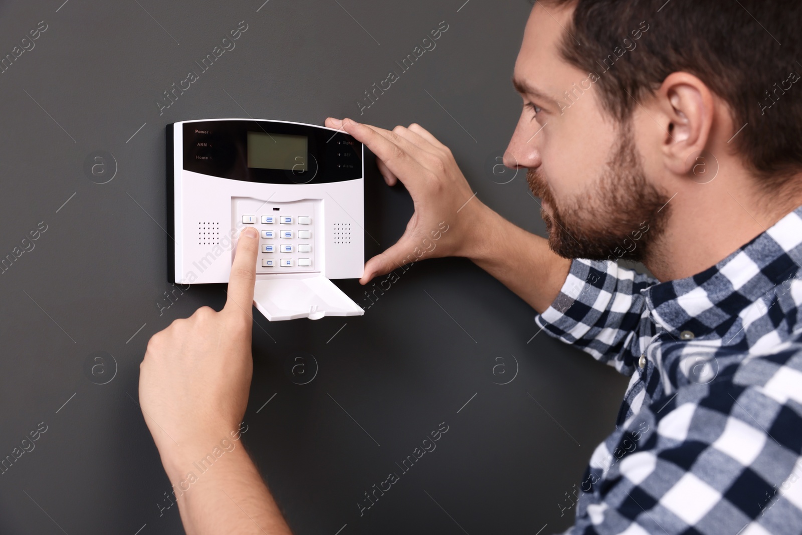 Photo of Man entering code on home security alarm system near gray wall