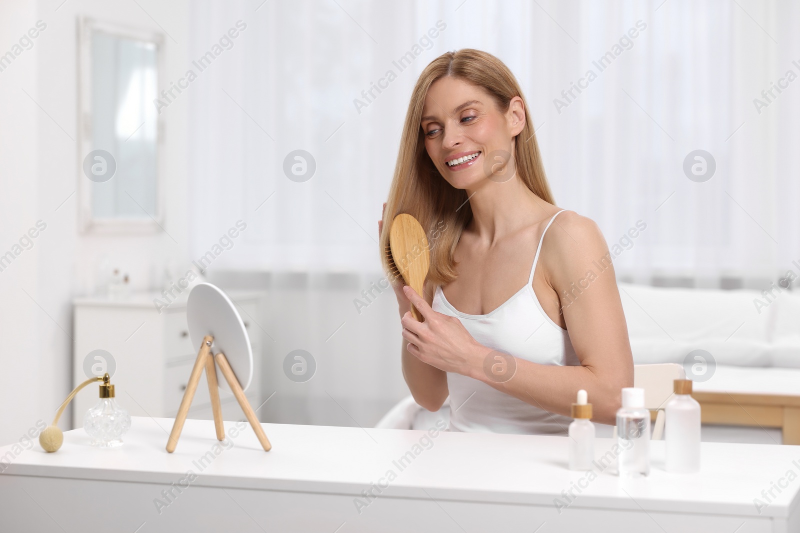 Photo of Beautiful woman brushing her hair at vanity in bedroom