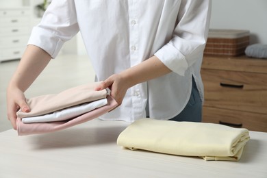 Photo of Woman folding clothes at white wooden table indoors, closeup