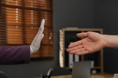 Photo of Woman refusing handshake from coworker at workplace, closeup