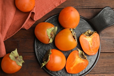 Photo of Tasty ripe persimmons on brown wooden table, flat lay