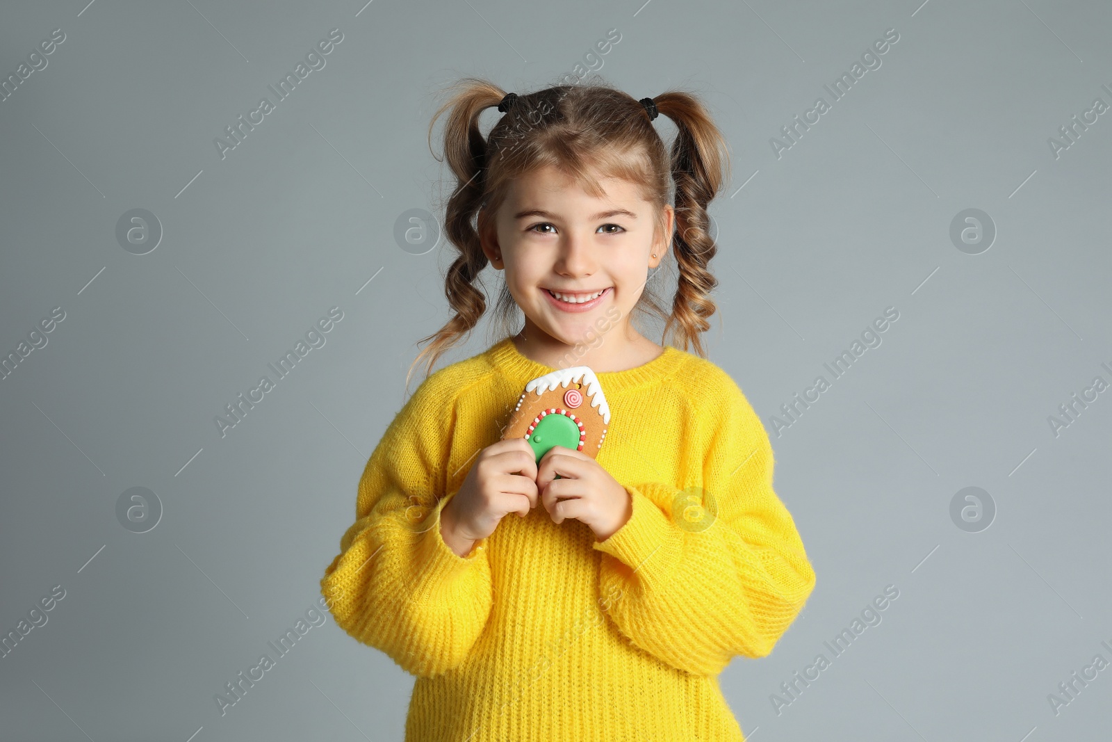 Photo of Cute little girl with Christmas gingerbread cookie on light grey background