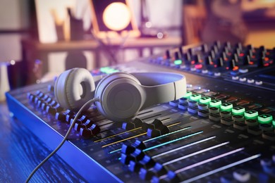 Photo of Professional mixing console with headphones on table in radio studio, closeup