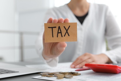 Woman holding card with word TAX at table