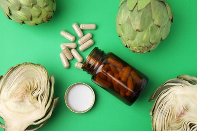 Photo of Bottle with pills and fresh artichokes on green background, flat lay