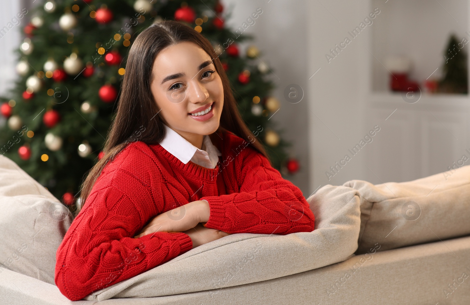 Photo of Portrait of smiling woman on sofa near Christmas tree at home