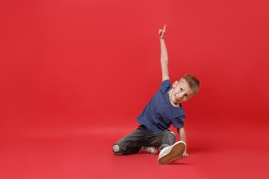 Photo of Happy little boy dancing on red background. Space for text