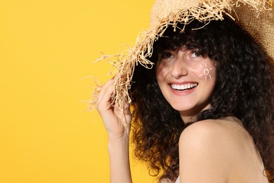 Beautiful happy woman in straw hat with sun protection cream on her face against orange background, space for text