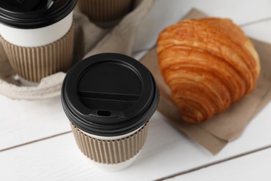 Photo of Coffee to go. Paper cups with tasty drink and croissant on white table, closeup