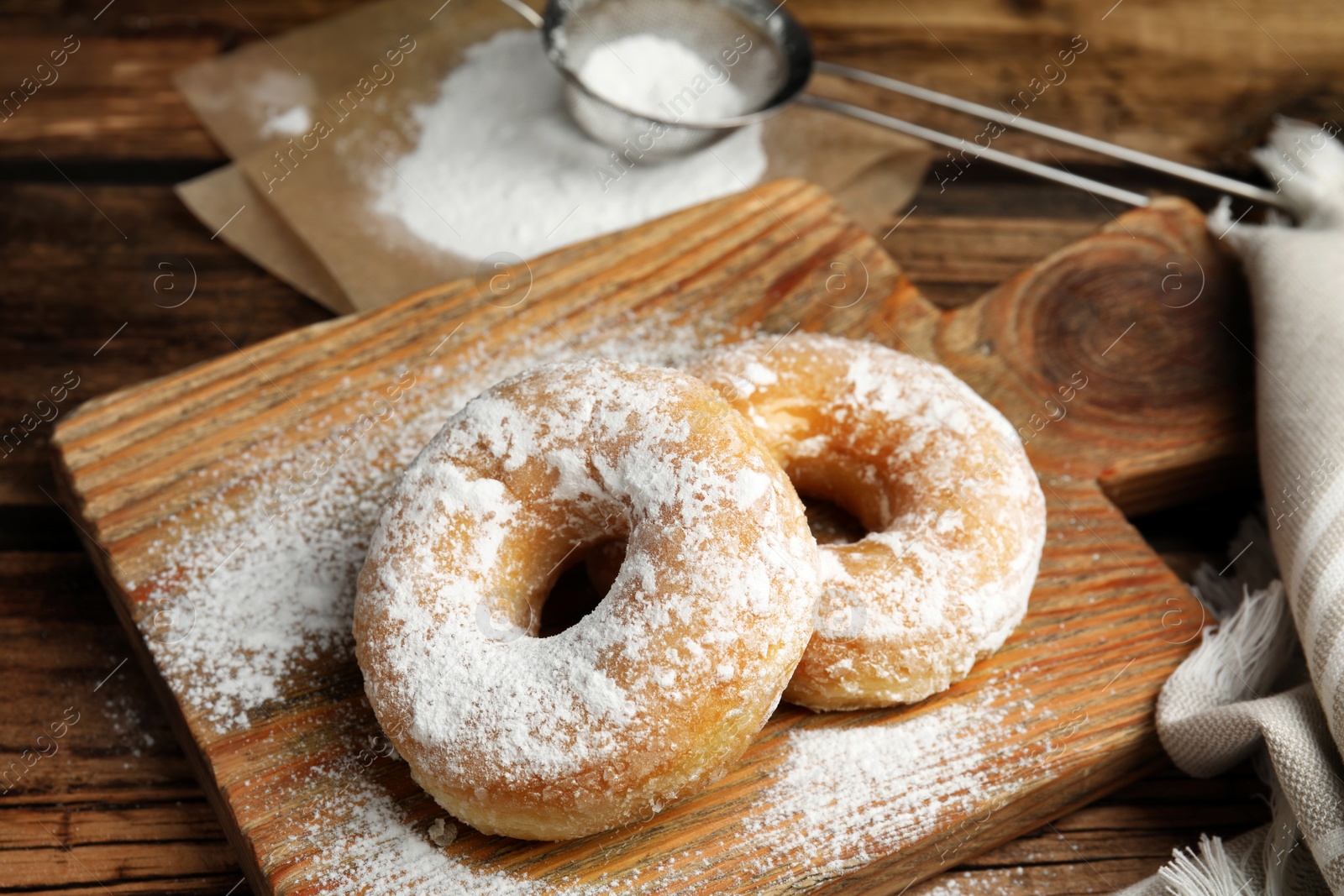 Photo of Delicious donuts with powdered sugar on wooden table