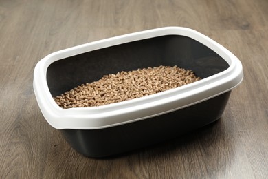 Photo of Cat litter tray with filler on wooden floor, closeup