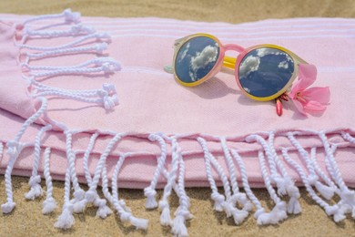 Blanket with stylish sunglasses and flower on sand outdoors, closeup. Beach accessories