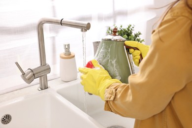 Woman washing electric kettle with sponge at sink in kitchen, closeup