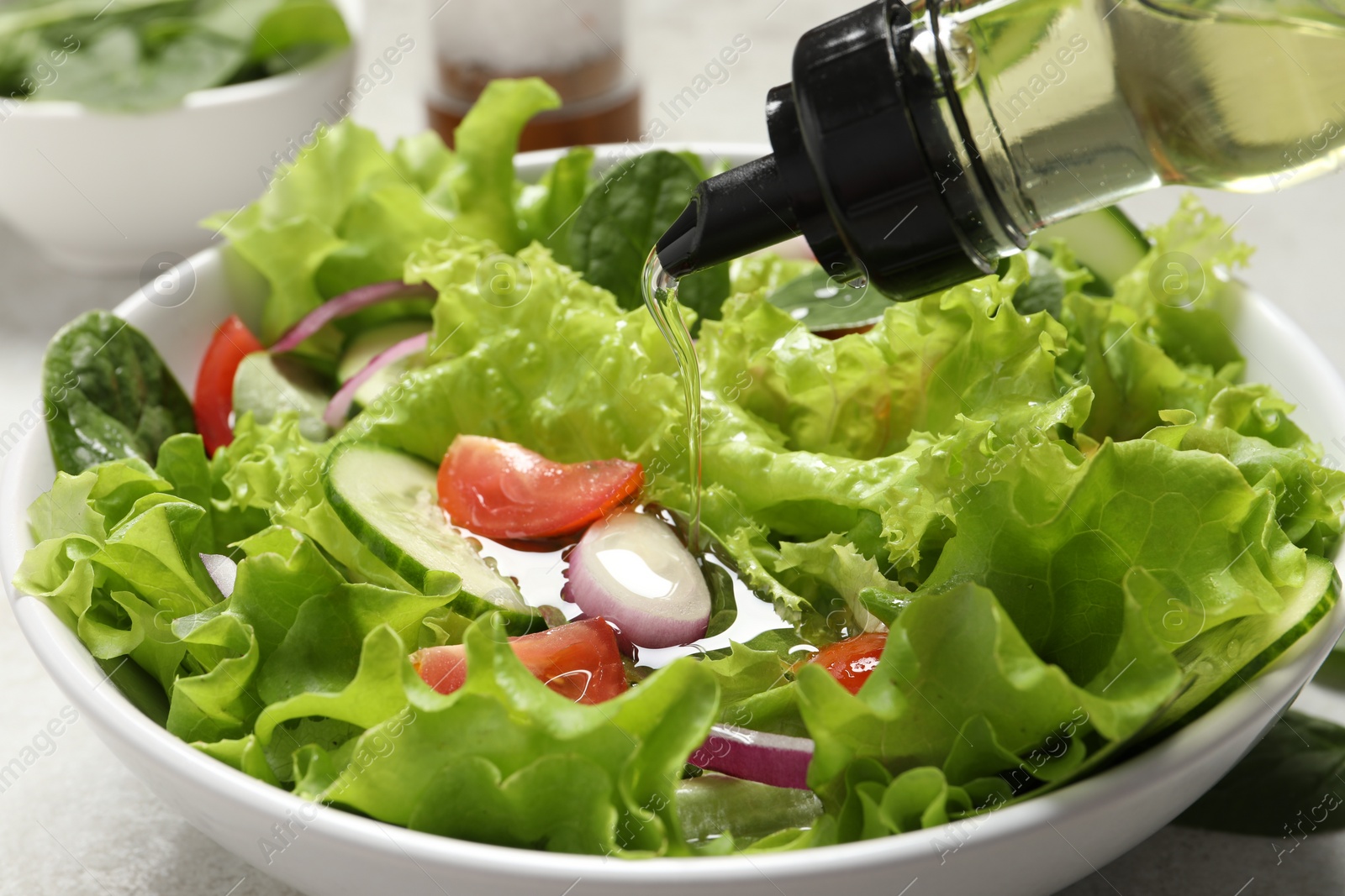 Photo of Pouring oil into salad on table, closeup