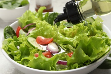 Photo of Pouring oil into salad on table, closeup
