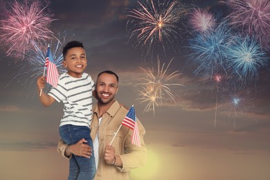Image of 4th of July - Independence day of America. Happy man and his son holding national flags of United States against sky with fireworks